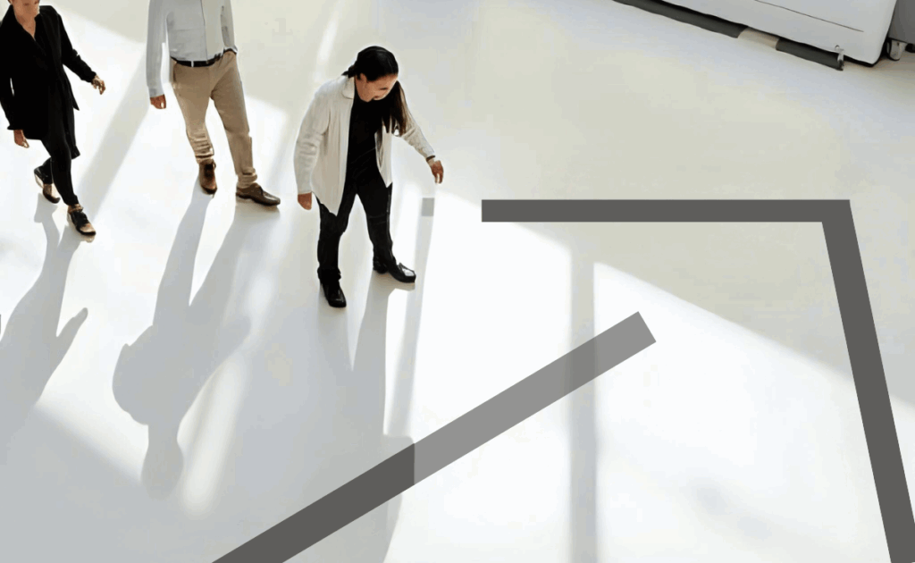 A group of professionals walking together in bright light across a minimalist floor, following a bold arrow graphic. The image symbolises alignment, shared direction, and collective movement — key qualities of a strong company culture guided by common purpose.